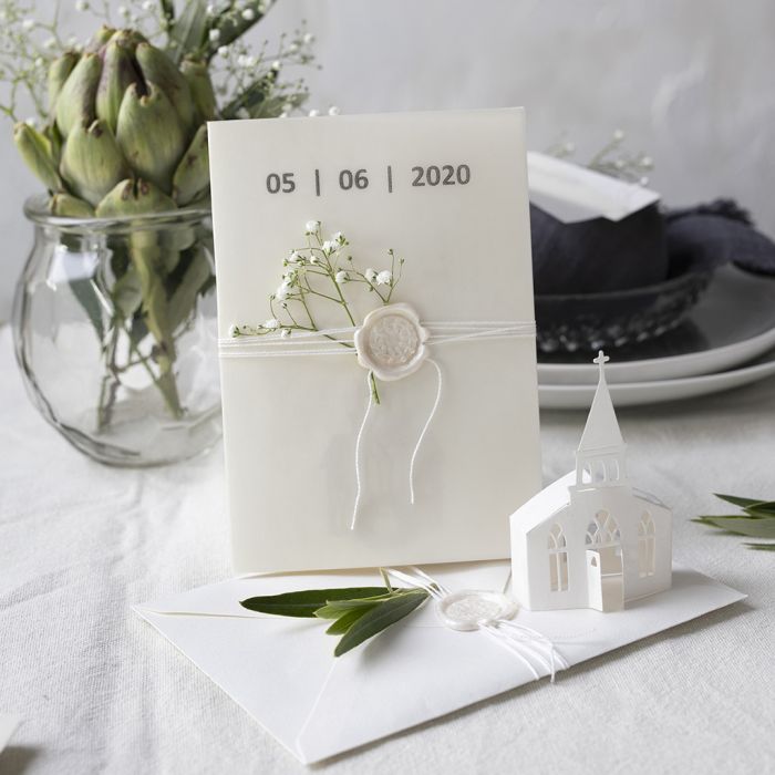 Une invitation dans des tons blanc cassé avec une église découpée à l’emporte-pièce et du papier calque.