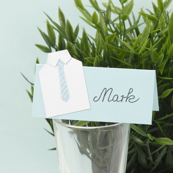 Une carte de placement pour une fête de confirmation avec une chemise en carton et une cravate en papier