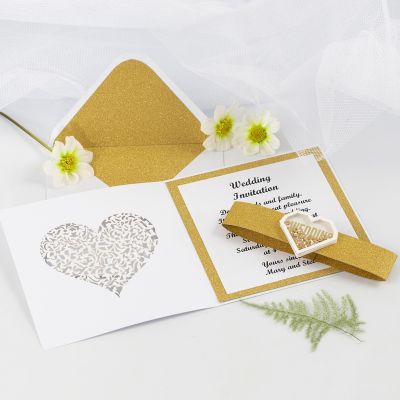 Une invitation de mariage avec du papier décoratif doré pailleté et un autocollant shaker en forme de cœur.
